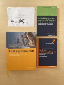 Erfahrungen mit AuDHD: Zu sehen ist ein Foto der Fachliteratur, die sich die Autorin für ihre Arbeit angeschafft hat. Darunter ist ein Lehrbuch der Erziehungswissenschaft, über die Ethik in der Behindertenpädagogik und über Heilpädagogisches Denken und Handeln. Zudem ist ein Flyer zur Einführung in die Unterstützte Kommunikation abgebildet.