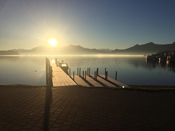 Therapieerfahrungen hochmaskierter Autismus: Zu sehen ist ein Bergsee im Sonnenuntergang. Der Himmel ist wolkenlos, man sieht einen Steg und Boote. Im Hintergrund sind die Berge. Es handelt sich um den See, an dem die erste Klinik der Autorin gelegen war.