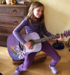 Leben mit AuDHD/ Doppeldiagnose Autismus und ADHS: Kinderfoto von Marlene mit ca. 9 Jahren. Sie ist komplett in lila gekleidet und spielt in einer Rockstarpose auf ihrer ebenfalls komplett lilafarbenen "Hannah Montana"-Gitarre.