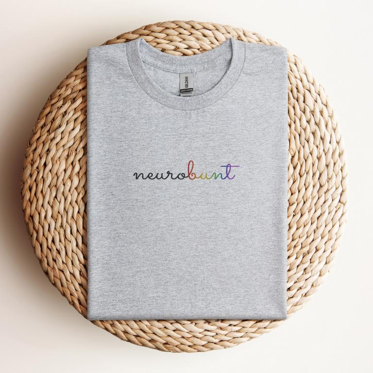 Gefaltetes T-Shirt mit handschriftlichem Aufdruck „neurobunt“ – minimalistisches Design für neurodivergente Menschen und neuroaffirmative Mode.