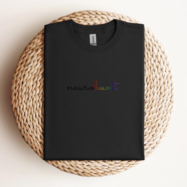 Gefaltetes T-Shirt mit handschriftlichem Aufdruck „neurobunt“ – minimalistisches Design für neurodivergente Menschen und neuroaffirmative Mode.